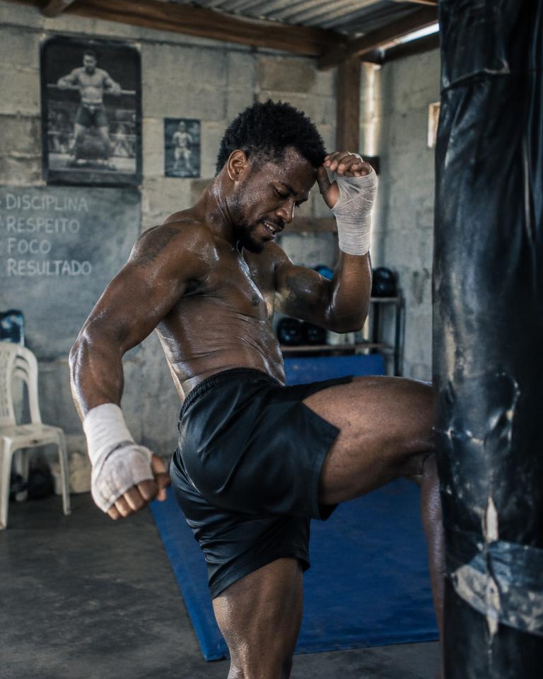 Lutador de MMA treinando chute em saco pesado em academia de bairro